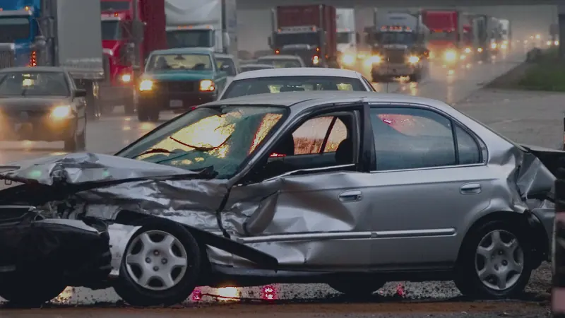 A car with heavy front-end damage on a wet highway after a collision