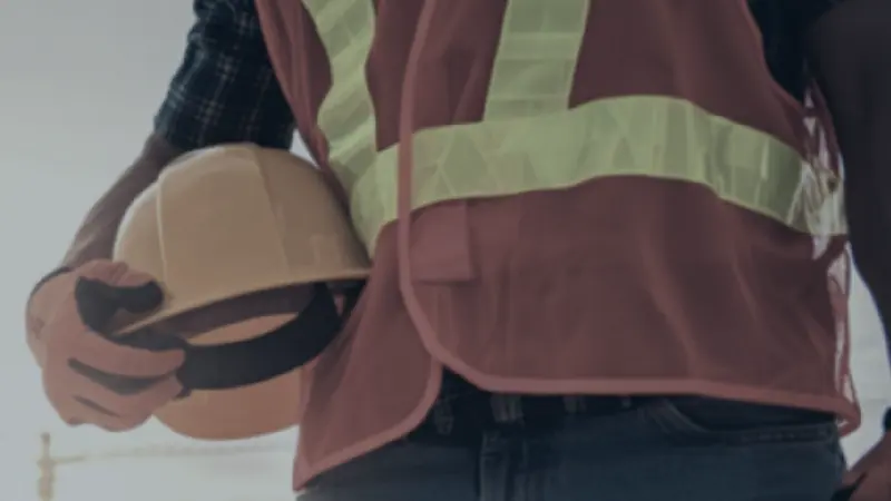 A construction worker in a high-visibility vest holding a hard hat